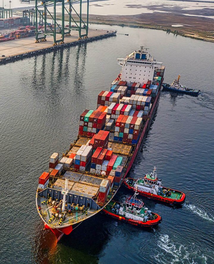 Aerial view of a container ship maneuvered by tugboats into port
